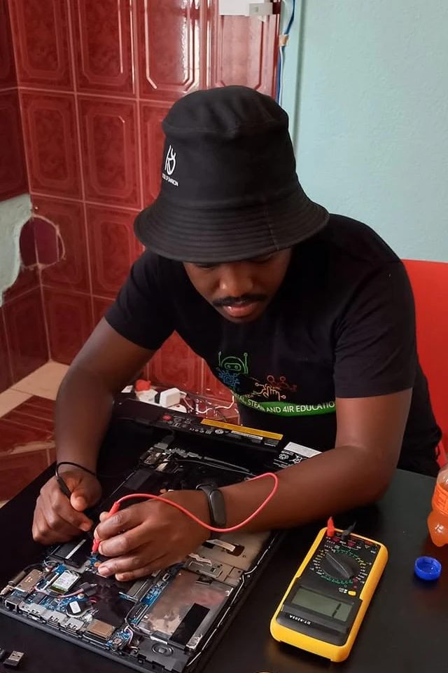 Thabiso Naleli working inside an open laptop with a multimeter and a tray of tools