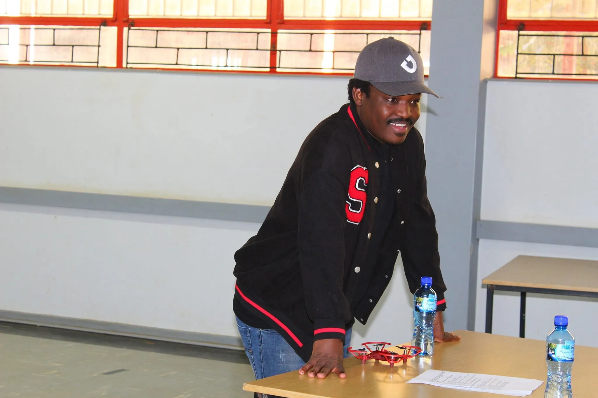 Thabiso Naleli leaning on a table in a classroom, smiling, with a small drone in front of him