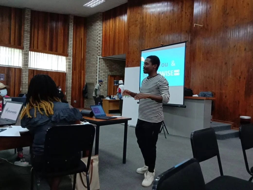 Thabiso Naleli facilitating a session in a hall with seated participants working on laptops